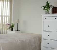 a bedroom with a bed, dresser and window in the corner that has vertical blinds