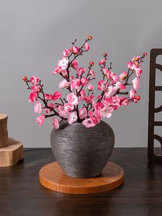 a vase with pink flowers in it sitting on a wooden stand next to a gray wall