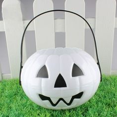 a white pumpkin shaped basket sitting on top of green grass next to a picket fence