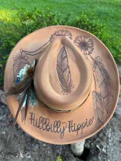 Hand burned sunflower and feather Hillbilly Hippie hat. This beauty is perfect for your next concert, dinner date or any special occasion. It's simply stunning. Hats are one size fits all with a drawstring to adjust sizing. Top Hat For Kentucky Derby And Country Events, Feathered Brimmed Hat Bands For Summer, Brimmed Hat Bands With Feathers For Summer, Feathered Hat Bands For Country Events In Summer, Feather Hat Bands For Country Events In Summer, Summer Hat Bands With Feathers For Country Events, Vintage Feather Hat Bands For Festival, Country Style Costume Hat For Events, Adjustable Feather Hats For Country Events