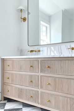 a bathroom with a marble counter top and wooden drawers under a large mirror on the wall