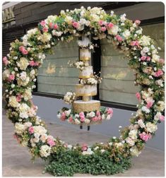 a wedding cake is surrounded by flowers in front of a store window on a city street