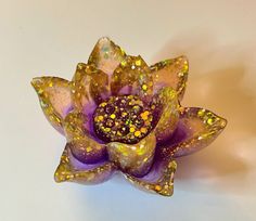 a purple flower with gold flecks on it sitting on a white table top