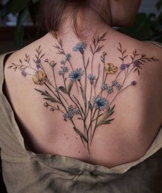 the back of a woman's shoulder with blue flowers on her left and yellow daisies on her right side