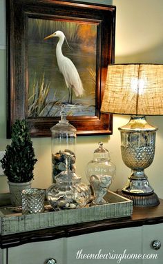 a white bird sitting on top of a table next to a lamp and vases