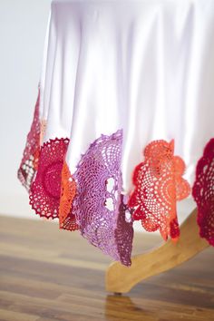 the table cloth is covered with colorful crochet doily and sits on a wooden stand