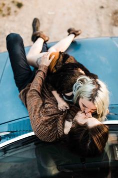 a man and woman laying on the hood of a blue car with their hands in each other's pockets