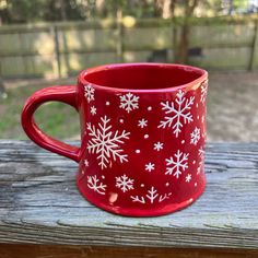 a red mug with white snowflakes on it sitting on a wooden table outside