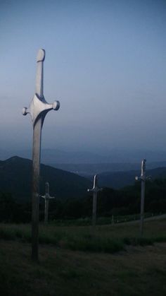 three crosses in the middle of a grassy field with mountains in the background at dusk