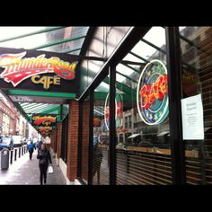 people walking down the sidewalk in front of a restaurant with neon signs on it's windows