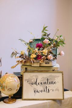 an adventure awaits sign sitting on top of a table next to a globe and flowers