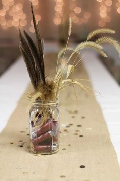 there is a vase with feathers in it on the long table runner, along with candles and confetti