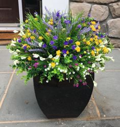 a potted planter filled with lots of flowers sitting on top of a sidewalk