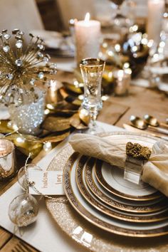 the table is set with gold and white plates, napkins, silverware, and candles