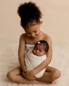 a baby wrapped in a blanket is sitting on the floor with her mother's arm around her