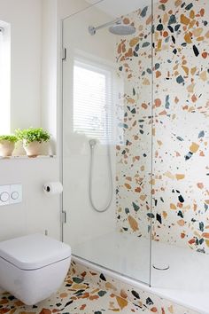 a white toilet sitting next to a shower in a bathroom with colorful tiles on the walls