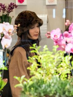 a woman wearing a fur hat looking at flowers