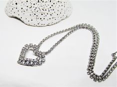 "A pretty vintage 1950's silver heart pendant necklace with sparkling crystals. It features a open heart pendant with a double row of glimmering clear pave rhinestones. The pendant is attached to a sparkling cup chain with tiny prong-set rhinestones. The chain is 14\" choker length with an additional 1\" length to adjust it longer. The clasp is a hook set with a pretty, sparkling crystal. The style would compliment most outfits and be perfect for everyday as well as special occasions. A perfect, Silver Rhinestone Necklace For Wedding On Valentine's Day, Silver Heart Rhinestone Necklace For Wedding, Silver Heart-shaped Rhinestone Necklace For Wedding, Silver Heart Shaped Rhinestone Necklace For Wedding, Silver Rhinestone Heart Pendant Necklace For Wedding, Silver Heart Pendant Rhinestone Necklace For Weddings, Heart-shaped Rhinestone Necklace For Wedding And Valentine's Day, Vintage Heart Pendant Necklace For Party, Vintage Heart Necklace For Valentine's Day Party