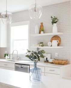 a kitchen with white cabinets and gray tile backsplash, plants in vases on the counter