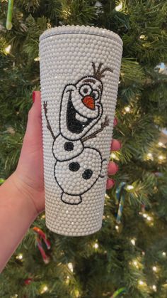 a hand holding a frosted cup with a cartoon character drawn on it in front of a christmas tree