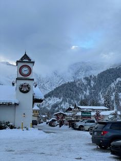 a clock tower in the middle of a parking lot with snow on the ground and mountains in the background