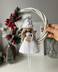 a hand holding a christmas ornament in front of a wreath