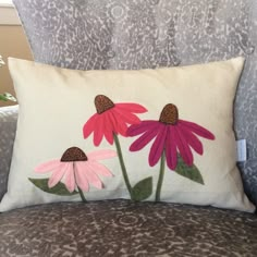 two pink flowers on a white pillow sitting on a gray couch next to a leopard print chair