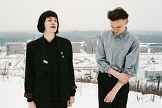 two people standing next to each other in the snow with buildings in the back ground