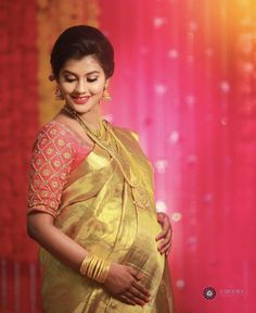 a pregnant woman in a yellow sari poses for the camera with her hands on her belly