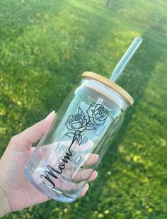 a hand holding a clear tumbler with the word mama written on it and two roses