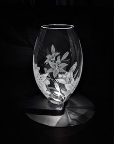 a glass vase with flowers etched on the side in black and white, against a dark background