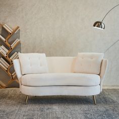 a white couch sitting in front of a tall book shelf next to a floor lamp