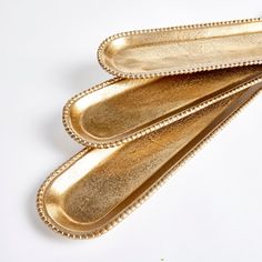 three gold serving spoons sitting next to each other on a white surface with beaded edges