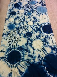 blue and white tie - dyed table runner with black circles on the center, in front of a wooden floor