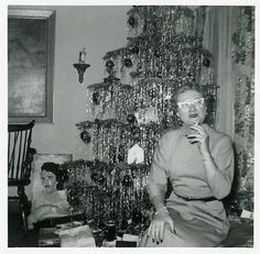 an old black and white photo of a woman sitting in front of a christmas tree