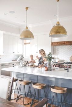 a woman standing in a kitchen next to two stools and a counter with food on it