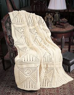 a white crocheted blanket sitting on top of a chair next to a lamp