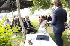 a bride and groom sitting under an umbrella at their outdoor wedding ceremony in the shade