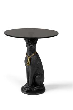 a black cat sitting on top of a table with a gold chain around it's neck