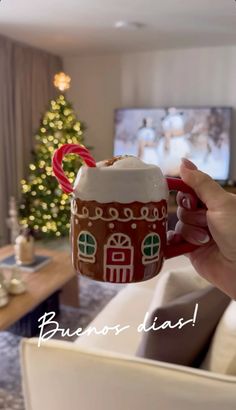 a hand holding a mug with a house on it and a candy cane sticking out of the cup