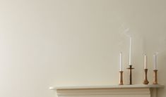 three candles are lit on top of a mantel in a room with white walls