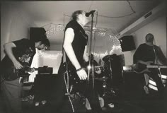 black and white photograph of three men playing guitars in a room with string lights on the ceiling