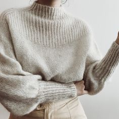 a woman wearing a white sweater and khaki pants with her hand on her hip