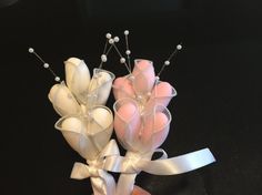 two small white and pink flowers on a black surface with ribbon around them, being held by someone's hand