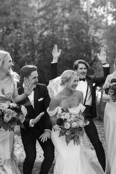 a group of people standing next to each other in front of trees and bushes with their hands up