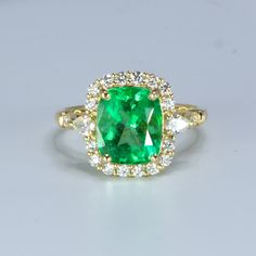 A magnificent Natural Colombian Emerald Statement Ring designed in 18 carats yellow gold presents a breathtaking 2.99 carats Colombian emerald with an enchanting vivid green colour. The emerald, featuring cushion cut, is surrounded by a gorgeous diamond halo. A pear cut diamond is delicately place at the start of the shank on each side and is followed by some more brilliant cut diamonds to elevate the design.  SPECIFICATIONS: 1982562 Central stone: One cushion cut natural Colombian Emerald.  10.01 x 8.36 x 5.8mm approx. Weight: 2.99 carats. Side Stones:  EF Diamonds TCW: 0.55 *2 x 3.7x2.5 Pear cut Diamonds.  *16 x 1.7mm Round Brilliant cut Diamonds.  *2 x 1.5mm Round Brilliant cut Diamonds.  *2 x 1.2mm Round Brilliant cut Diamonds.  *2 x 0.9mm Round Brilliant cut Diamonds.  Material: 18K Y Elegant Green Emerald Ring With Halo Setting, Exquisite Green Emerald Ring With Halo Setting, Luxury Cushion Cut Emerald Ring, Luxury Green Cushion Cut Jewelry, Luxury Green Radiant Cut Rings, Green Emerald Ring With Halo Setting, Baguette Cut, Luxury Green Emerald Ring For May Birthstone, Cushion Cut Emerald Green Rings, Green Baguette Cut Emerald Ring With Halo Setting