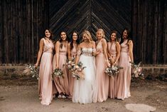 a group of women standing next to each other in front of a barn door holding bouquets