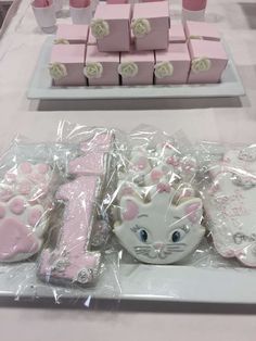 there are many pink and white cakes on the table with cat cookies in plastic wrappers