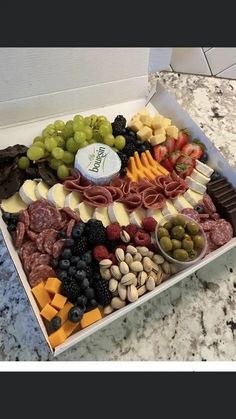 an assortment of cheeses, meats and fruit in a box on a counter