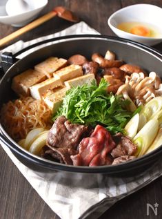 a bowl filled with meat and vegetables next to chopsticks on a wooden table